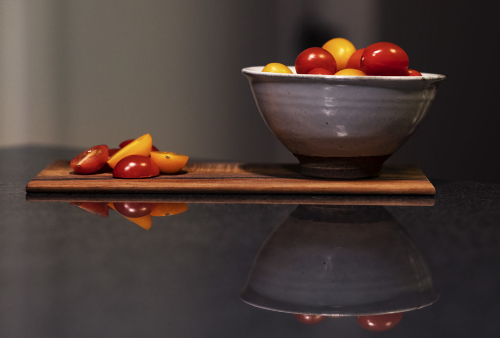 Bowl of red and orange cherry tomatoes sitting next to a pile of cut cherry tomatoes